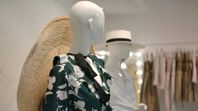 Pan left shot of white dummies in stylish outfits, including hats with brim against elegant interior of showroom in light clothing shop.