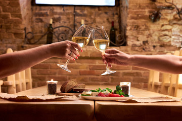 Female's hands toasting with glasses of white wine over table. Women's friendship