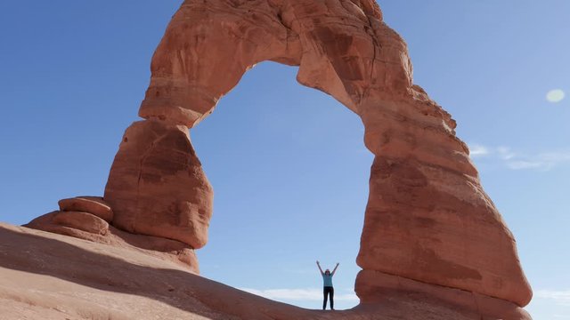 Woman Raises Her Hands Up In Delicate Arch Of Orange Rock In National Park