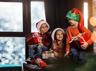 Obraz premium Little children with Christmas gifts near window indoors. Presents from Santa Claus