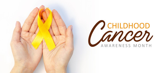 Top view female hands hold gold ribbon symbol of Childhood cancer awareness. Wide banner with text...