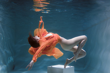 Beautiful girl swims underwater in a yellow dress. 2020 New Year trend Aqua Mente and fatom blue...