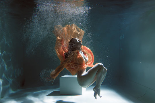 Beautiful girl swims underwater in a yellow dress. 2020 New Year trend Aqua Mente and fatom blue and lush lava. Underwater girl mermaid. Model suitable for advertising