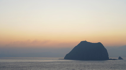 Naklejka na ściany i meble Rock on the background of the sunset sky. orange yellow sky. foggy sunset in the ocean