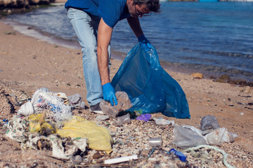 Man volunteer with big bag for trash collecting garbage on beach. Environmental pollution concept