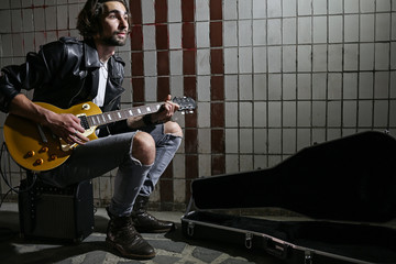 Street musician sitting on the amplifier and playing guitar in the underpass. Vagrant lifestyle....