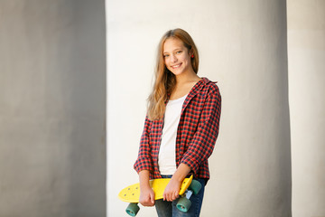 Lifestyle outdoor portrait of young smiling teenage girl with a yellow skateboard