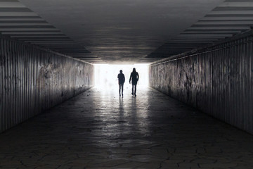 man and woman walk in a dark tunnel towards the light