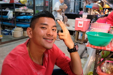 Fototapeta premium Selective focus,teenage Asian men handsome, braces, tan skin, red shirt, smiling, raising two fingers, happy in the Chinatown market at night.