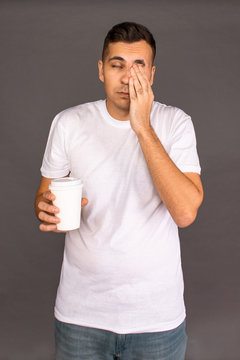 A guy in a white t-shirt is drinking coffee and trying to Wake up and cheer up.