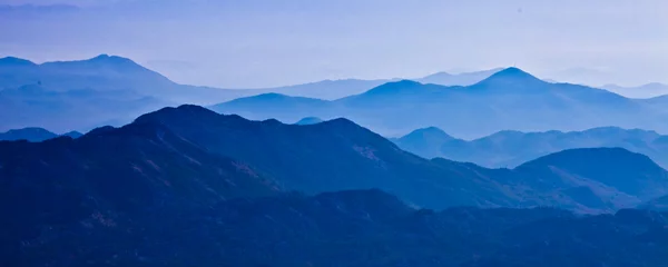 Fototapeten mit blauen, nebligen, geheimnisvollen Bergen in der Ferne und einem orangefarbenen Pastellhimmel. Ferne blaue Berge. © Mikhail Semenov