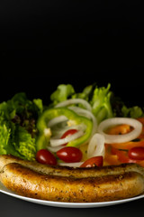 Two long grilled bratwurst sausage with mix vegetables salad in the white plate isolated on black background