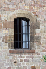 Fototapeta na wymiar Arched Window with Iron Bars Set in Masonry Wall of Stone Blocks 
