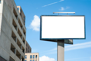 Blank white billboard mockup and modern apartmen building with concrete facade against blue sky