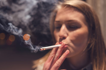 Obraz premium Close up portrait of young caucasian woman smoker on the street at night with cigarette smoking in the city outdoor smoke enjoining