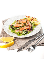 green salad with red fish and vegetables on a kitchen towel with cutlery on a white background isolated
