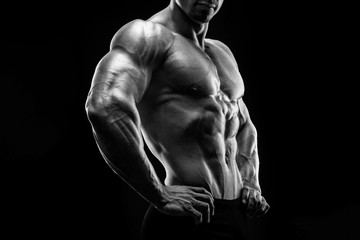 Muscular and fit young bodybuilder fitness male model posing over black background. Black and white photo.