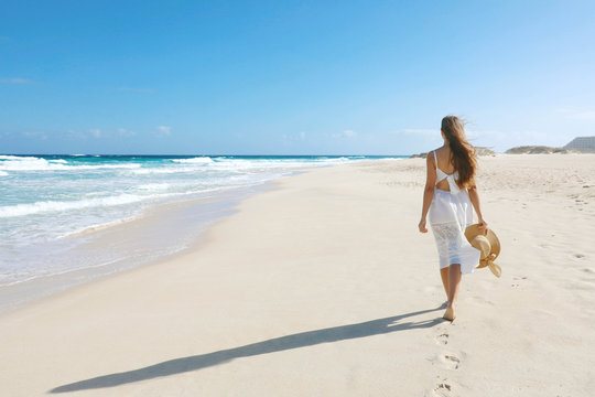 Young woman walking on empty wild beach with white sand and blue sky in Corralejo, Canary Islands