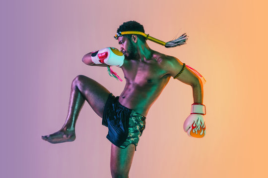 Muay thai. Young man exercising thai boxing on gradient background in neon light. Fighter practicing, training in martial arts in action, motion. Healthy lifestyle, sport, asian culture concept.