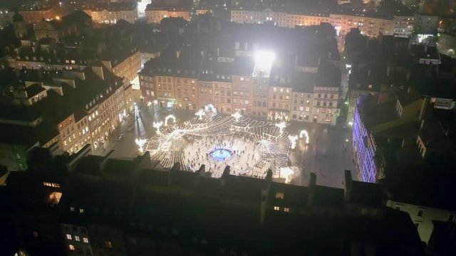 Drone shot at a night rink with beautiful lighting and people.  Aerial view of the old city in winter at night with people skating.