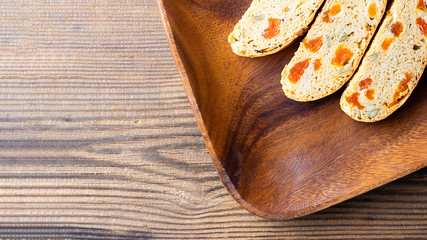 Three pieces of Biscotti with Apricot and Pumpkin seeds on square brown wooden plate on textured bachground, Horizontal banner, top view shot with copy space. Italian traditional sweet dried bread,