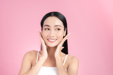 Beautiful young Asian girl touching her perfect skin on pink background. Skin care concept