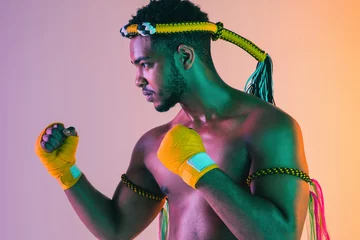 Fotobehang Muay thai. Young man exercising thai boxing on gradient background in neon light. Fighter practicing, training in martial arts in action, motion. Healthy lifestyle, sport, asian culture concept. © master1305