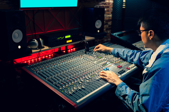 asian professional producer, sound engineer working on audio mixing console in recording, broadcasting studio