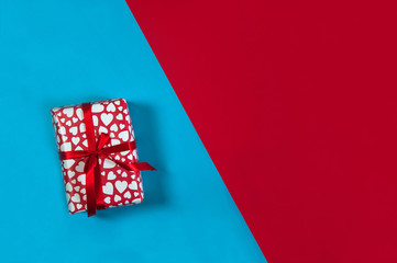The concept of Valentine's Day in a minimalist style. The gift box is decorated with ribbons on a red and blue background. Free space for your text.