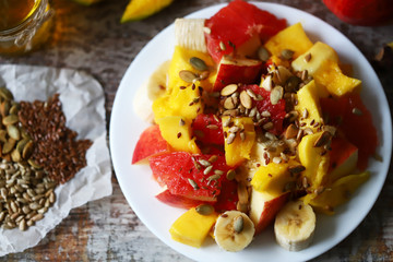 Fruit salad on a white plate. Healthy salad with fruits, honey and seeds. Healthy dessert. Proper nutrition concept. Selective focus. Macro.