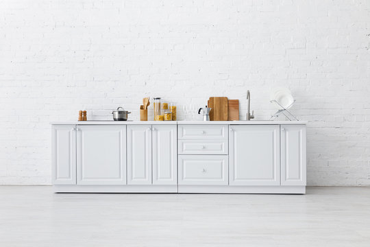 Fototapeta minimalistic modern white kitchen interior with kitchenware near brick wall