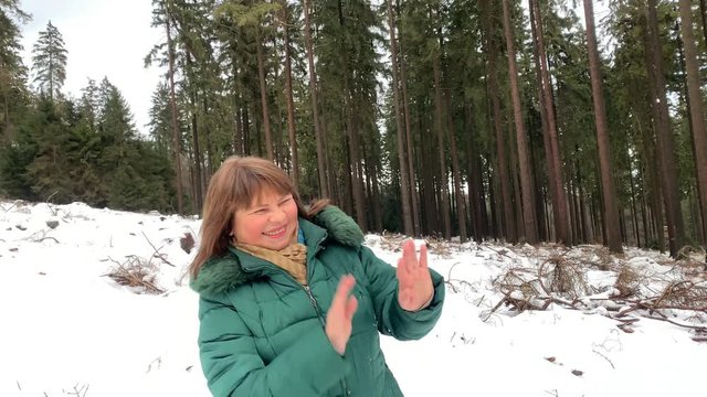 middle-aged woman in jackets in winter in a snowy forest fooling around fooling around, playing snowballs, concept of sporty, healthy lifestyle