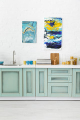 modern white and turquoise kitchen interior with kitchenware and abstract paintings on brick wall