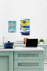 selective focus of laptop and pot on induction cooktop with kitchenware and abstract paintings on background