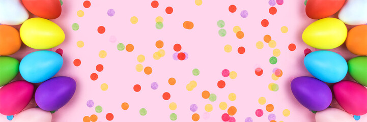 Banner made from colored Easter eggs on pink background with confetti. Flat lay.