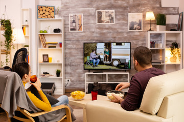Back view of couple in living room watching a movie on the TV