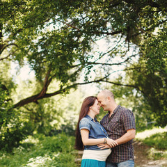 Man and pregnant woman, embracing in park outdoors