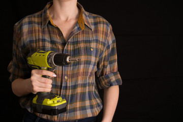 A girl in a work shirt holds a screwdriver in her hands, a symbol of feminism, on a black background