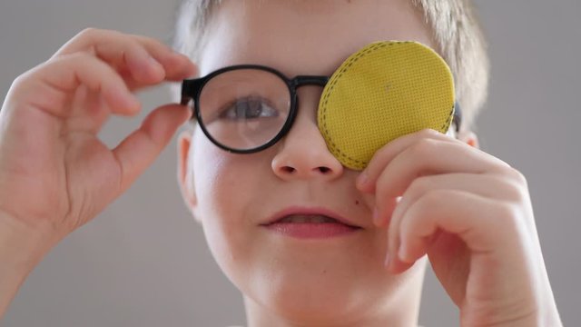 Portrait of funny child in new glasses with yellow spot to correct strabismus Orthopedic Boys Eye Patches nozzle for glasses for treatment of strabismus (lazy eye). Boy puts on and corrects glasses
