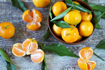 Selective focus. Ripe juicy tangerines with leaves in a bowl. Peeled tangerines. Tangerines in a peel.