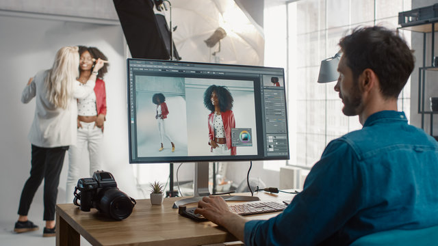 Backstage of the Photoshoot: Make-up Artist Applies Makeup on Beautiful Black Girl. Photo Editor Works on Desktop Computer Retouching Photo with Image Editing Software. Fashion Magazine