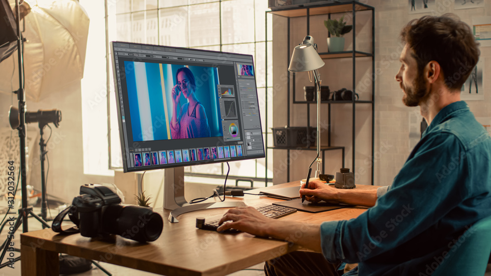 Poster professional photographer sitting at his desk uses desktop computer in a photo studio retouches. aft