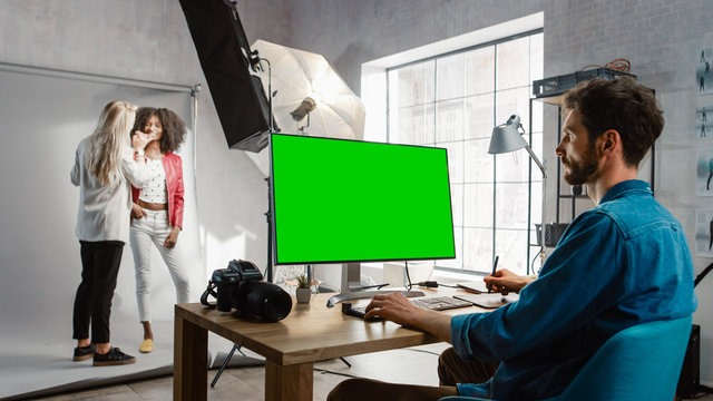 Backstage of the Photoshoot: Make-up Artist Applies Makeup on Beautiful Black Girl. Photo Editor Works on Desktop Computer with Green Mock-up Screen Display. Fashion Internet Magazine 