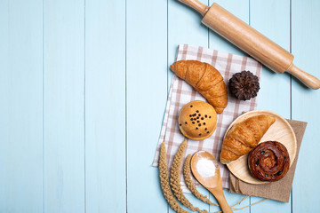 Bakery background frame.Homemade breads or bun, croissant and Rolling pin, Whisk ,flour on blue wood background,top view and copy space.