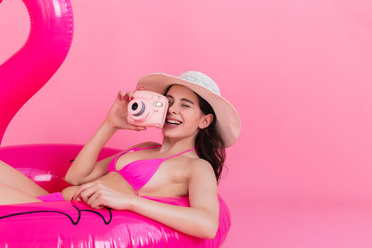 The girl in a swimsuit lies on an inflatable flamingo and takes a photo on the instant camera
