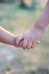 A romantic image of an older sister's hand holding her brother's hand together.