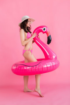 The girl in a swimsuit and hat holds a flamingo and posing in the studio