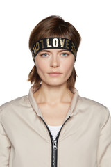Close-up shot of sporty European woman in a beige zippered jacket and with a black knitted headband with golden words "love". The girl is looking straight into the camera.  © RedUmbrella&Donkey