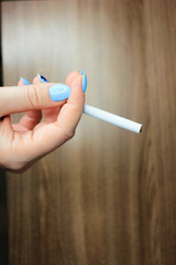 Hand of a young woman with one cigarette between fingers. White cigarette on a wooden table background in hand.