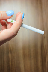 Hand of a young woman with one cigarette between fingers. White cigarette on a wooden table background in hand.